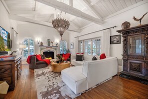 A spacious living room with a fireplace, white sofas, a wooden coffee table, and a large chandelier. - Sunset Vale (West Hollywood)