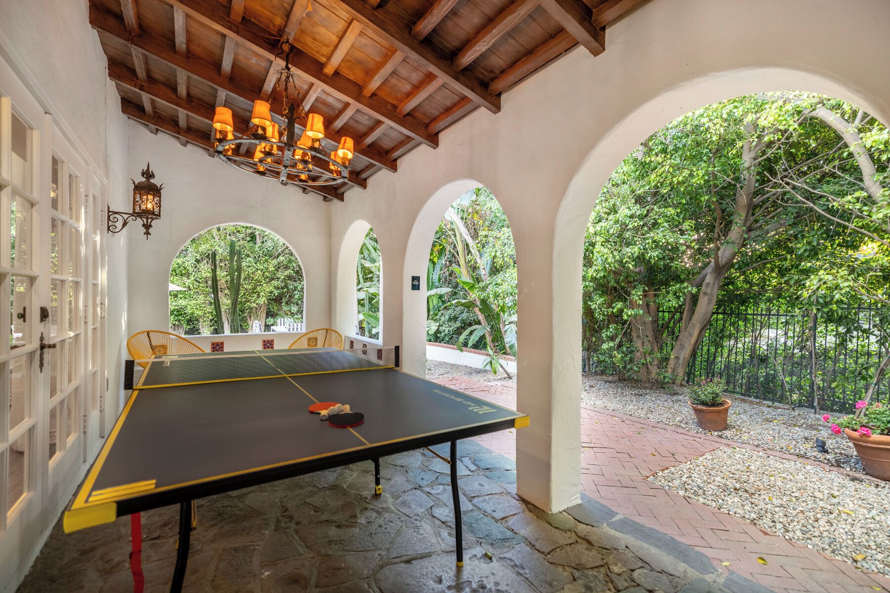 A ping pong table in an outdoor area with a wooden ceiling and arched windows.