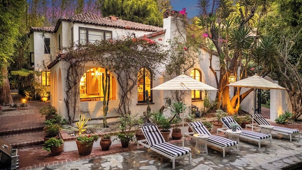 A villa with a patio area featuring lounge chairs and umbrellas, surrounded by potted plants and trees. - Sunset Vale (West Hollywood)