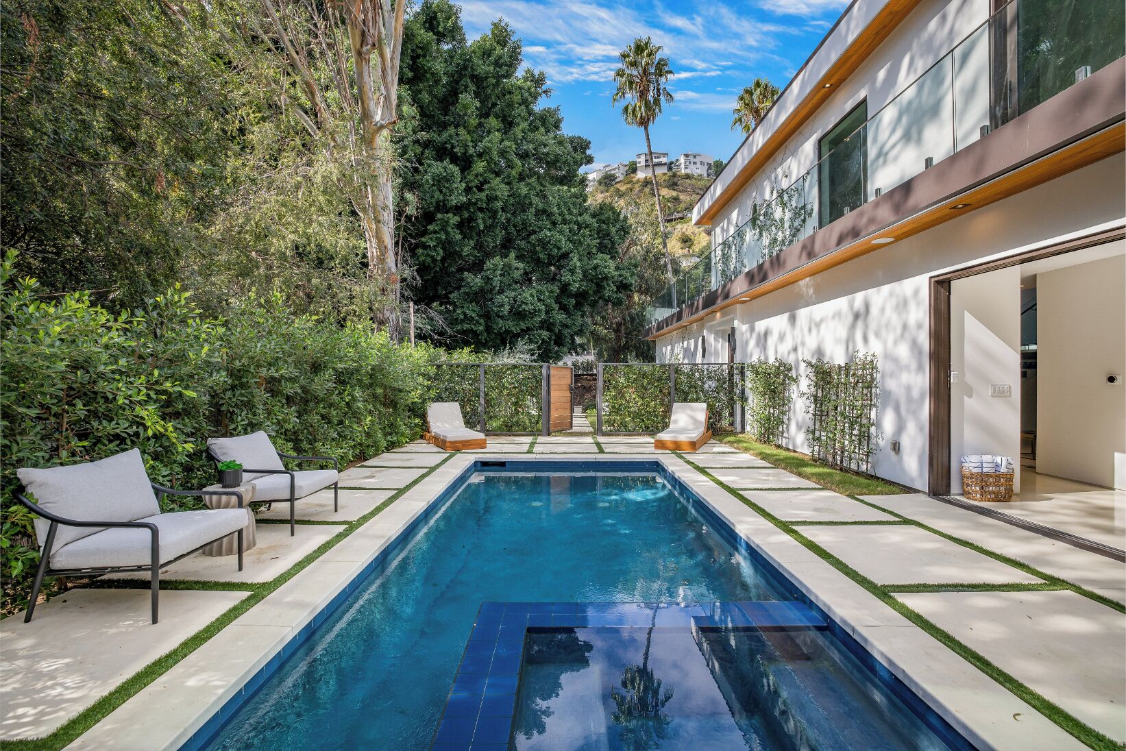 A modern pool area with a rectangular pool, two lounge chairs, and a small table.