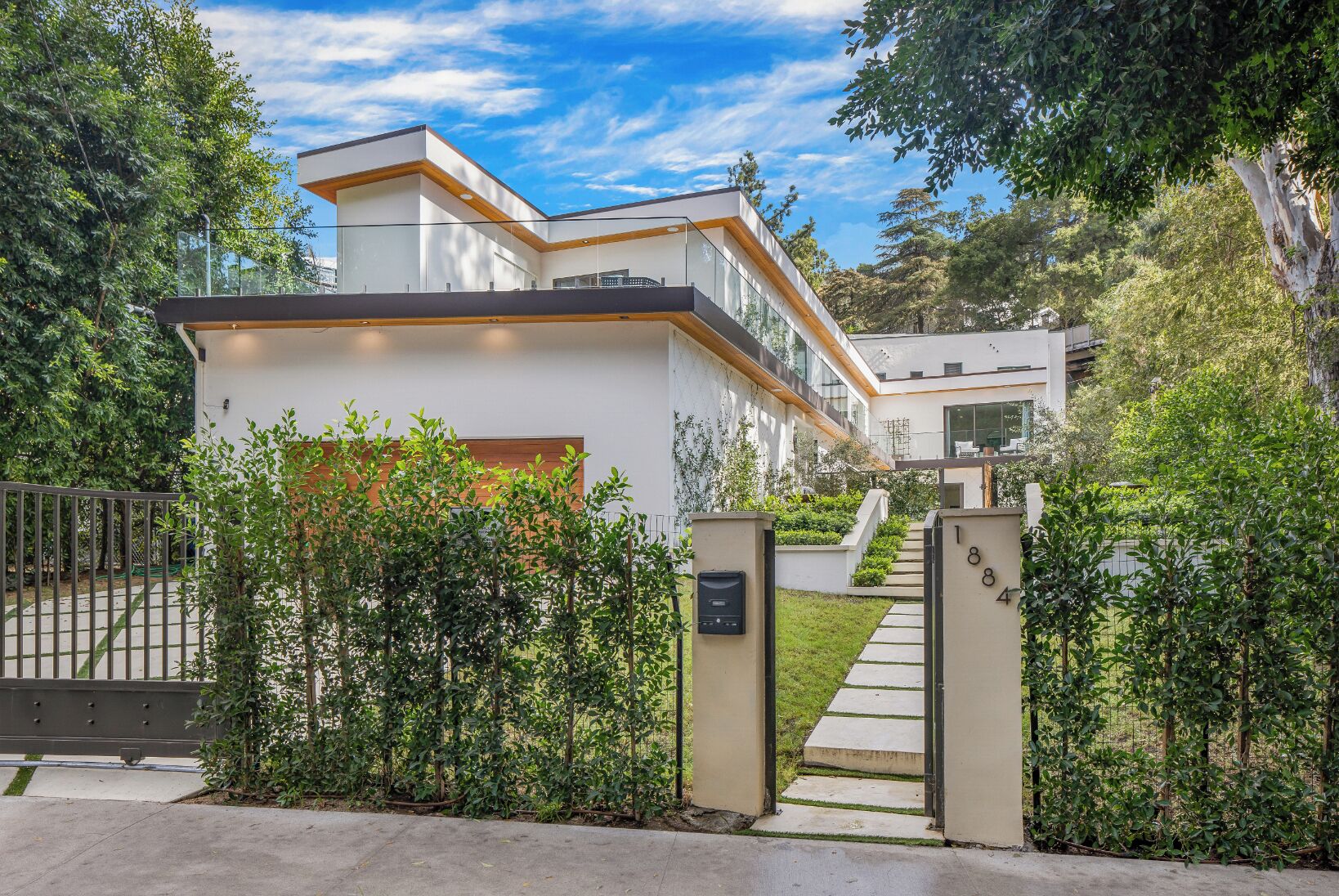 A modern residential building with a flat roof, large windows, and a well-maintained garden.