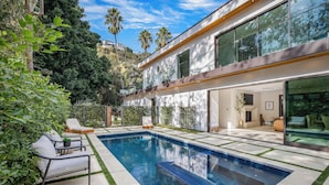A modern house with a swimming pool, outdoor seating, and a view of a hill with buildings. - Laurel Canyon (Los Angeles)