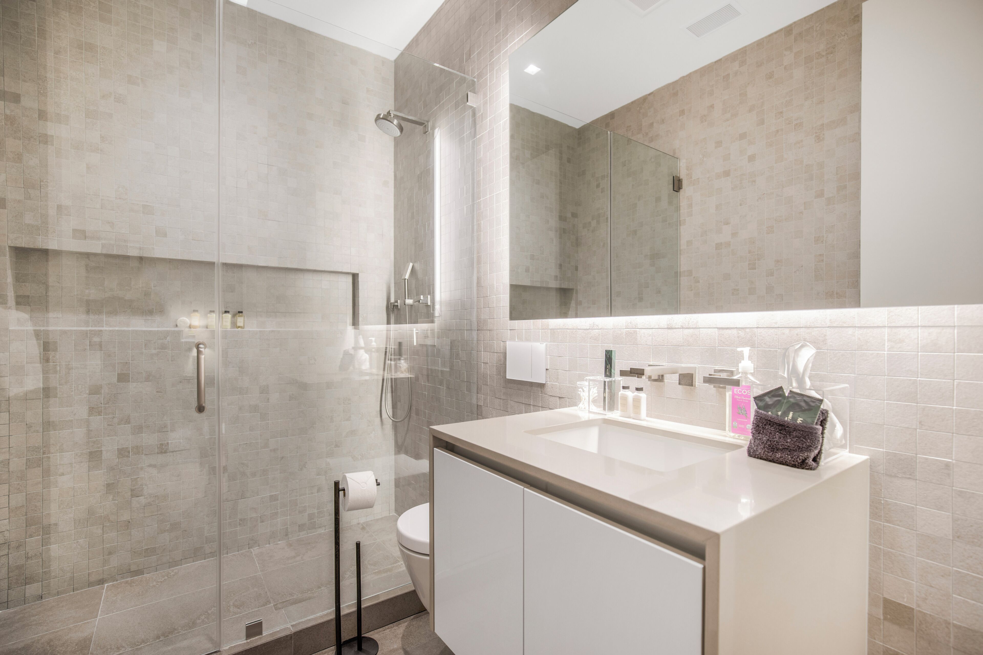 A modern bathroom with a glass-enclosed shower, a white sink with a mirror above, and a toilet.