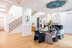 Ein großzügiger Essbereich mit Glastisch und modernen Stühlen, eine Treppe mit Holzwertungen und zeitgenössische Kunstwerke.