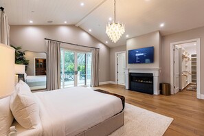 Ein geräumiges Schlafzimmer mit einem großen Bett, einem Kamin, einem Fernseher und einem Balkon mit Vorhängen.