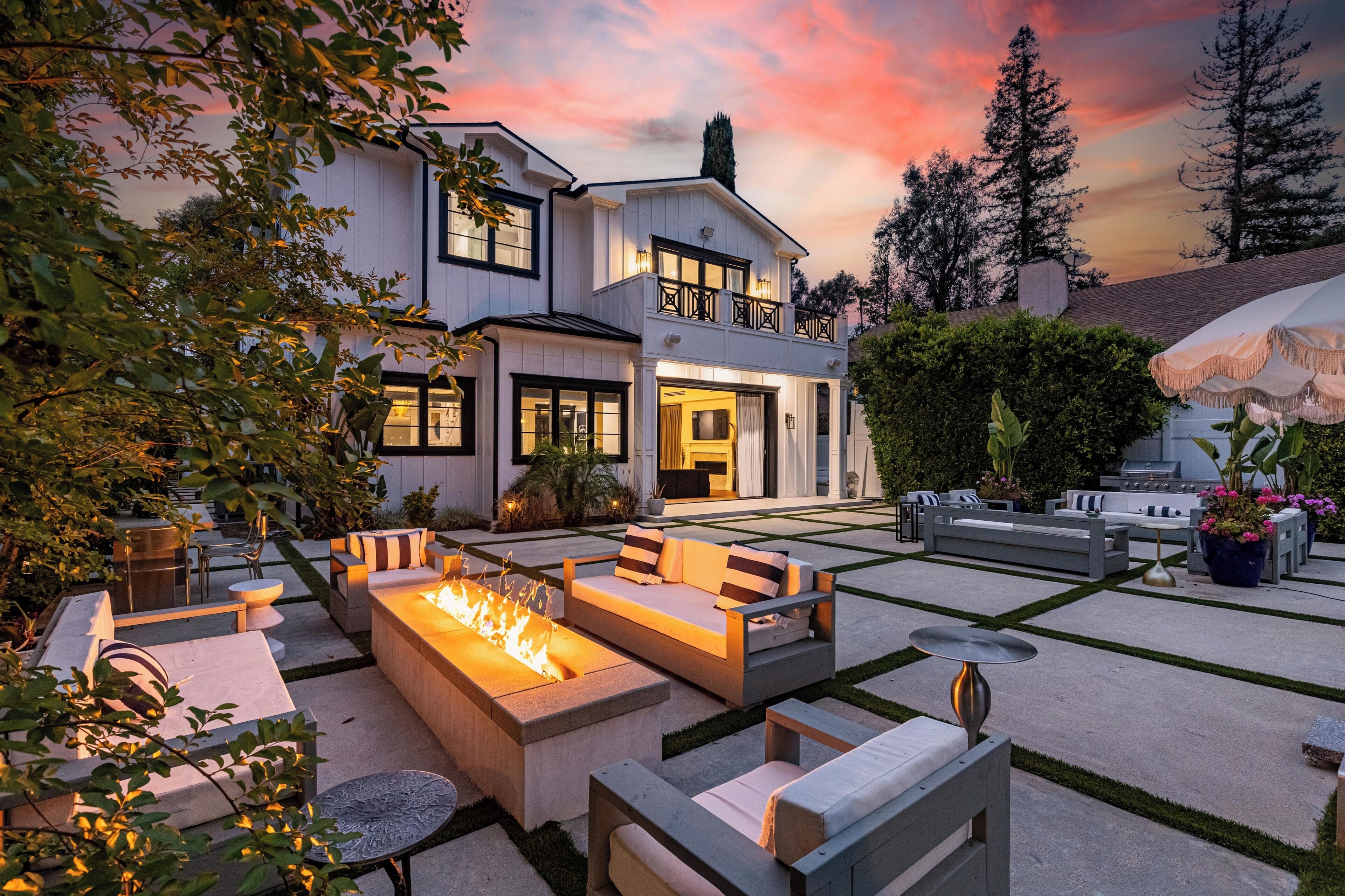 A modern house with a spacious outdoor patio featuring a fire pit, seating areas, and a well-maintained garden.