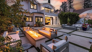 A modern house with a spacious outdoor patio featuring a fire pit, seating areas, and a well-maintained garden. - Otis Ave (Tarzana)