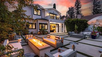 A modern house with a spacious outdoor patio featuring a fire pit, seating areas, and a well-maintained garden.