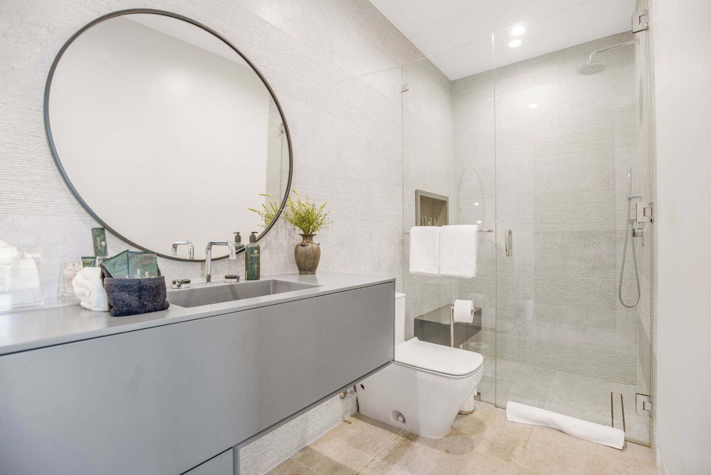 A modern bathroom with a large mirror, a sink, a toilet, and a glass-enclosed shower.