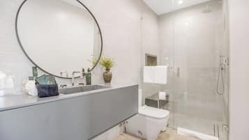 A modern bathroom with a large mirror, a sink, a toilet, and a glass-enclosed shower.