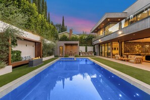 A modern outdoor pool area with a clear blue pool, surrounded by well-maintained grass and greenery. - Levitt Lane (Sherman Oaks)