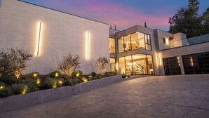 A modern two-story house with a flat roof, large windows, and a well-lit exterior.