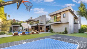 A modern house with a basketball court, outdoor seating, and a pool.