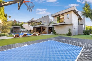 Una casa moderna con cancha de baloncesto, mobiliario exterior y piscina.