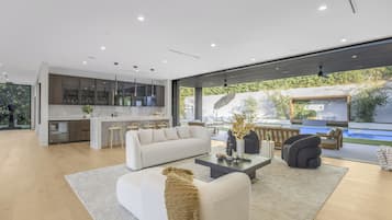 A modern living space with a kitchen, a white sofa, a coffee table, and a view of a swimming pool.