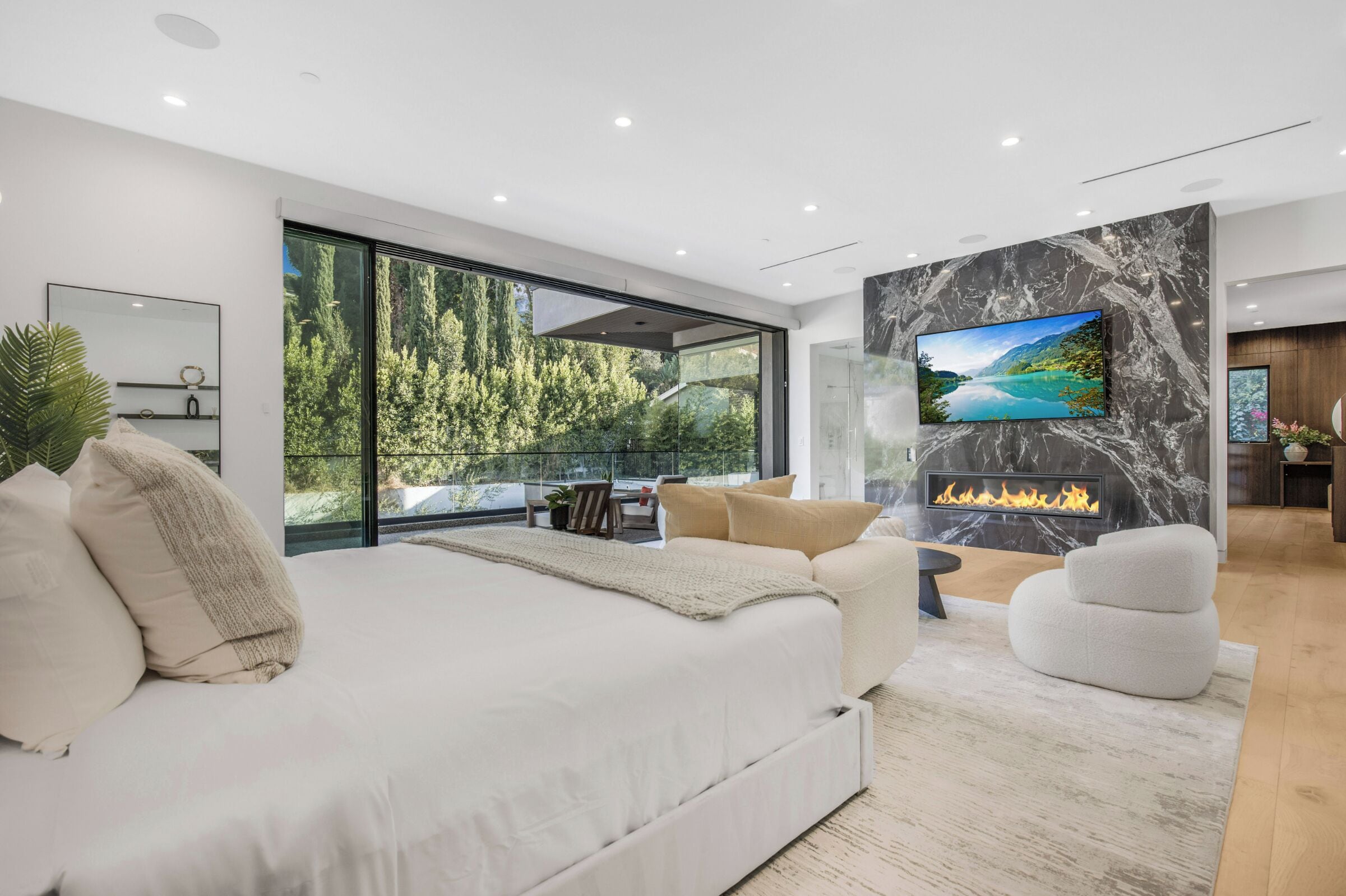 A modern bedroom with a large bed, a TV mounted on a marble wall, and a fireplace.
