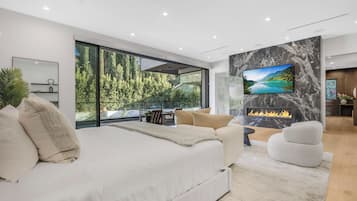 A modern bedroom with a large bed, a TV mounted on a marble wall, and a fireplace.