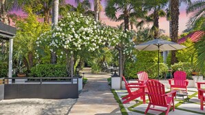 Un patio avec un jardin tropical, des chaises Adirondack rouges, un sentier et une pergola ornée de fleurs blanches.