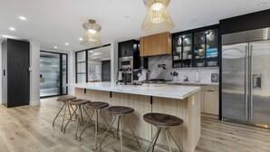 Une cuisine moderne dotée d’un grand îlot central, de tabourets de bar, d’appareils électroménagers en acier inoxydable et de luminaires suspendus.