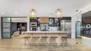 Une cuisine moderne dotée d’un îlot central, de tabourets de bar et de luminaires suspendus.