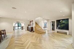 A spacious living area with a herringbone wood floor, a staircase, and a large abstract painting. - Bella Villa (Los Angeles)