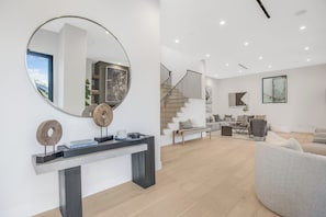 Un salon moderne doté d’un grand miroir rond, d’un escalier et d’un coin salon comprenant un canapé et des fauteuils.