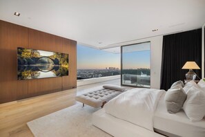 A modern living room with a large flat-screen TV, a sofa, a bench, and a view of a cityscape through large windows. - Collingwood (West Hollywood)