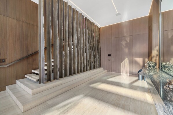 A modern interior with a staircase, wooden panel walls, and a glass table with decorative items. - Collingwood (West Hollywood)