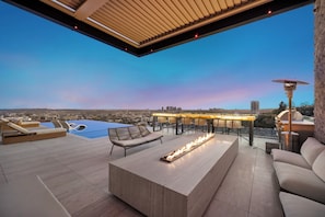 A rooftop terrace with a pool, lounge chairs, a fire feature, and a dining area with outdoor lighting. - Collingwood (West Hollywood)