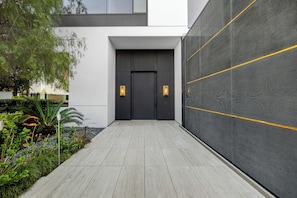A modern building entrance with a dark door, two wall-mounted lights, and a pathway leading to the entrance. - Collingwood (West Hollywood)