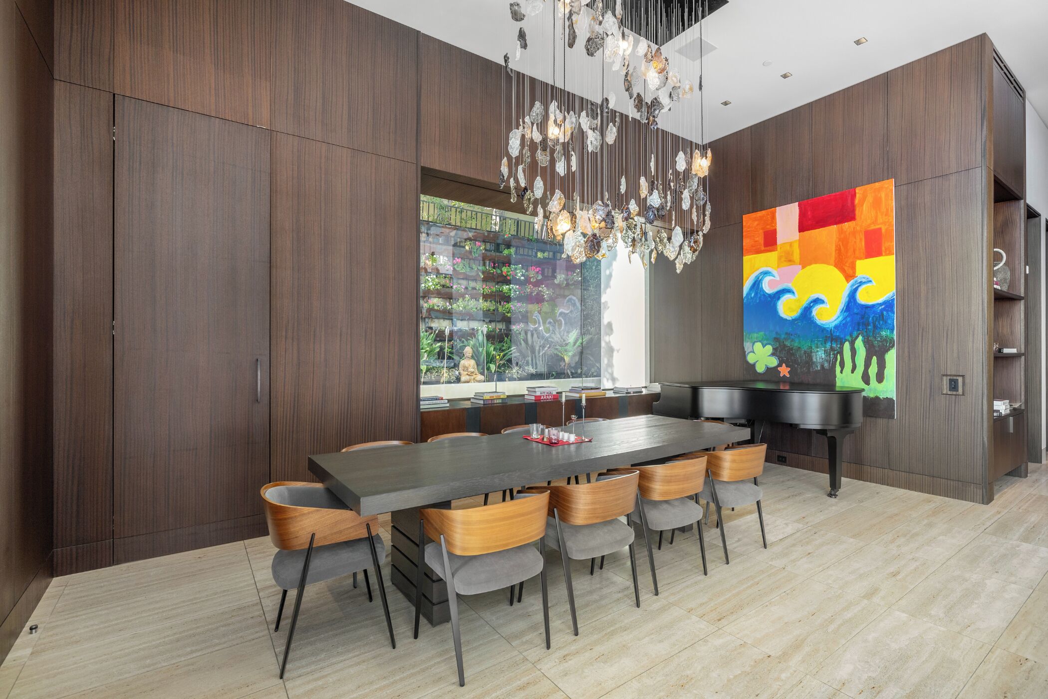 Uma sala de jantar moderna com uma mesa comprida, cadeiras, um candelabro e uma grande pintura abstrata.
