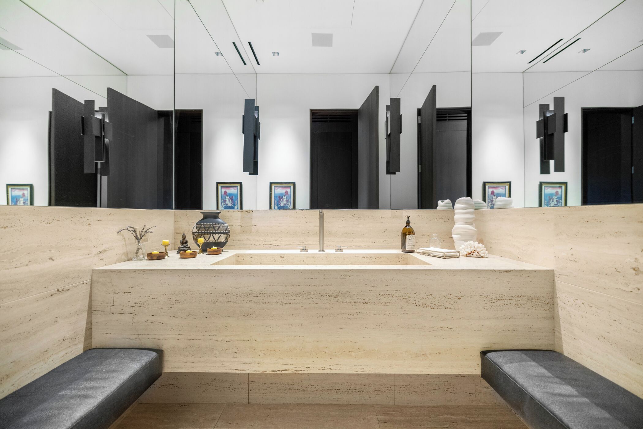 A modern bathroom with a large mirror, a sink, and two benches.
