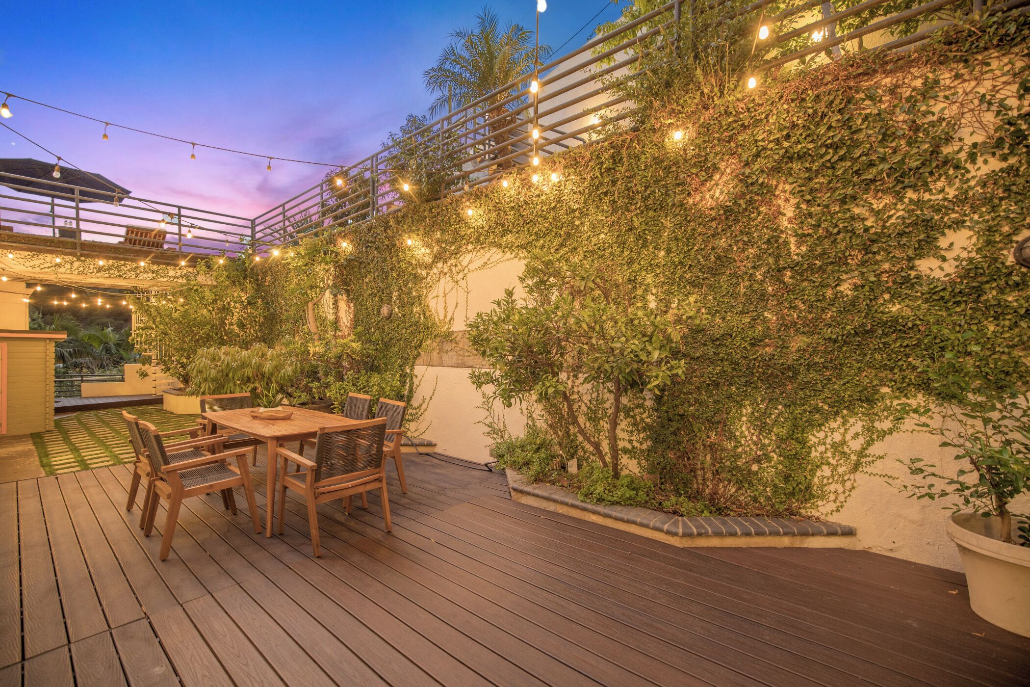 An outdoor patio with a wooden deck, a table with chairs, and string lights.