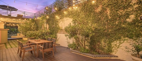 An outdoor patio with a wooden deck, a table with chairs, and string lights.
