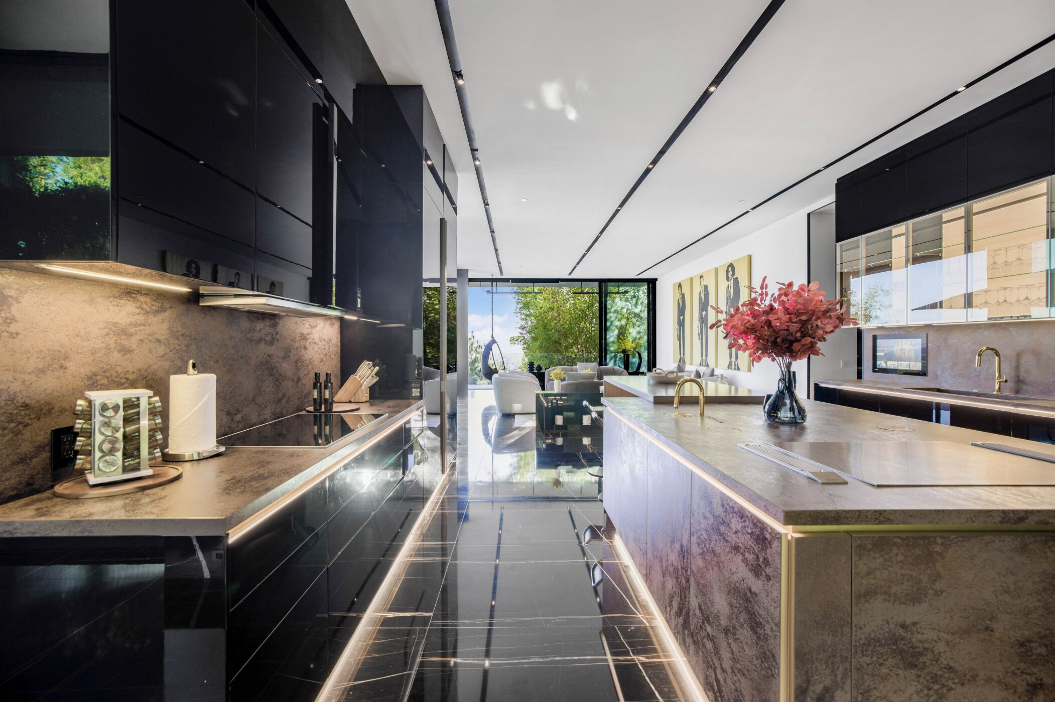 A modern kitchen with black cabinetry, a marble countertop, and a view of the outdoors.