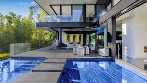 A modern outdoor pool area with a glass-enclosed deck, outdoor seating, and a view of the surrounding greenery. - London Dream (West Hollywood)