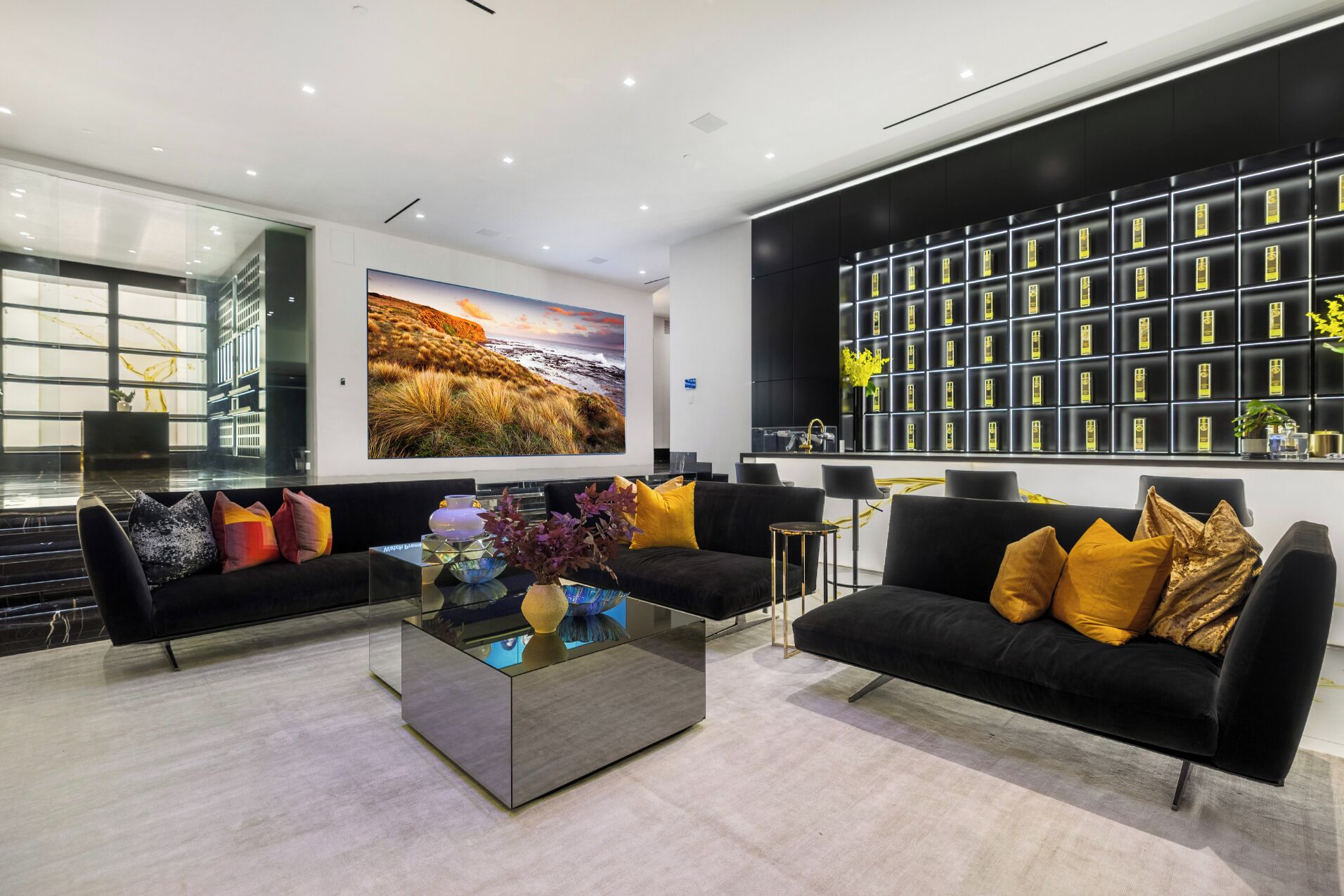A modern living room with black sofas, a glass coffee table, and a large painting of a landscape.