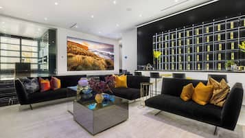 A modern living room with black sofas, a glass coffee table, and a large painting of a landscape.