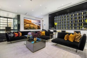 A modern living room with black sofas, a glass coffee table, and a large painting of a landscape. - London Dream (West Hollywood)