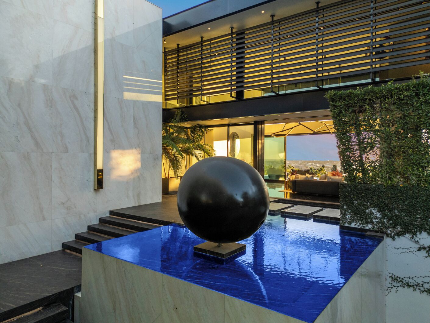 Un área de piscina interior moderna con una gran escultura esférica negra, un techo de cristal y vistas de la ciudad.