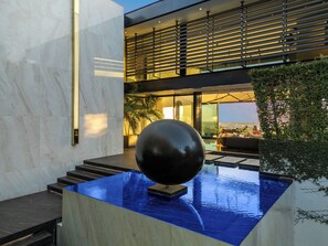 A modern indoor pool area with a large black spherical sculpture, a glass ceiling, and a view of the cityscape. - London Dream (West Hollywood)