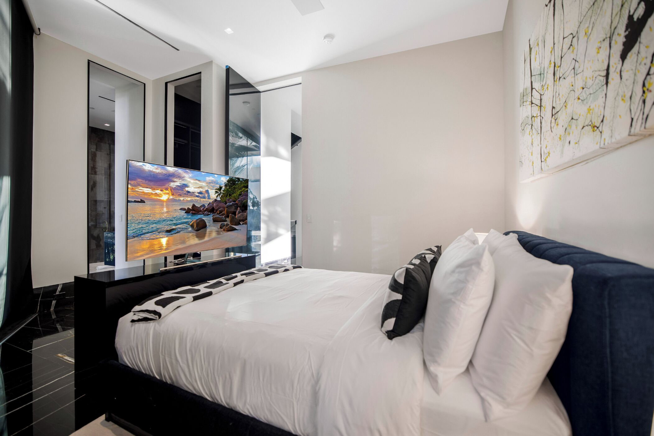 A modern bedroom with a large bed, a flat-screen TV, and a painting on the wall.