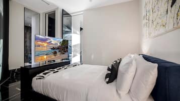 A modern bedroom with a large bed, a flat-screen TV, and a painting on the wall.