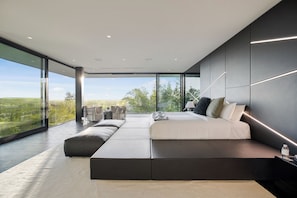 A modern bedroom with a large bed, a seating area, and a view of the countryside. - London Dream (West Hollywood)