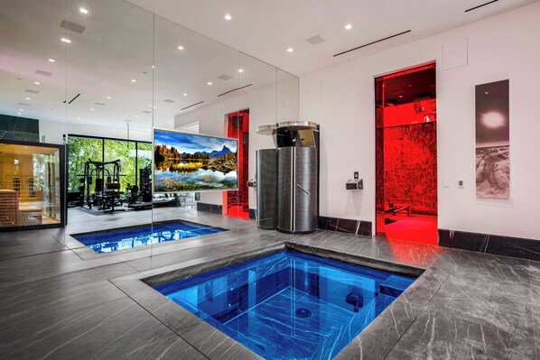 A modern indoor swimming pool with a glass wall, a sauna, and a gym area. - London Dream (West Hollywood)