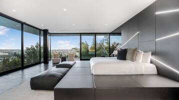 A modern bedroom with a large bed, a seating area, and a city view through large windows.