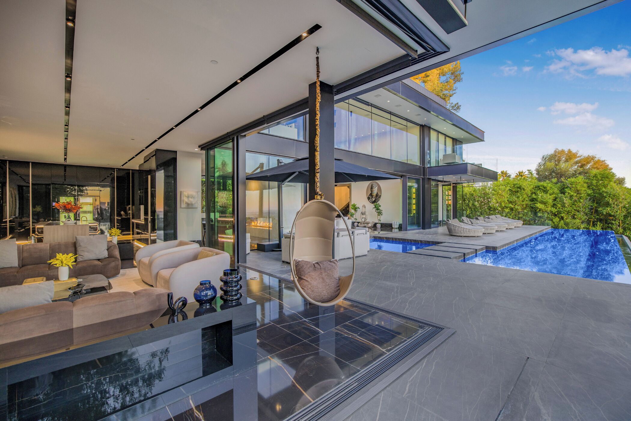 A modern living room with a hanging chair, a pool, and a view of the outside.