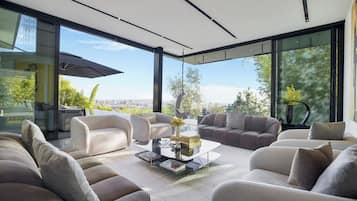 Una sala de estar moderna con una mesa de centro de vidrio, varios sofás y un amplio ventanal con vistas a la ciudad.