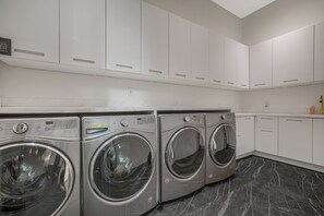 A laundry room with three front-loading washing machines, white cabinets, and a marble floor. - London Dream (West Hollywood)