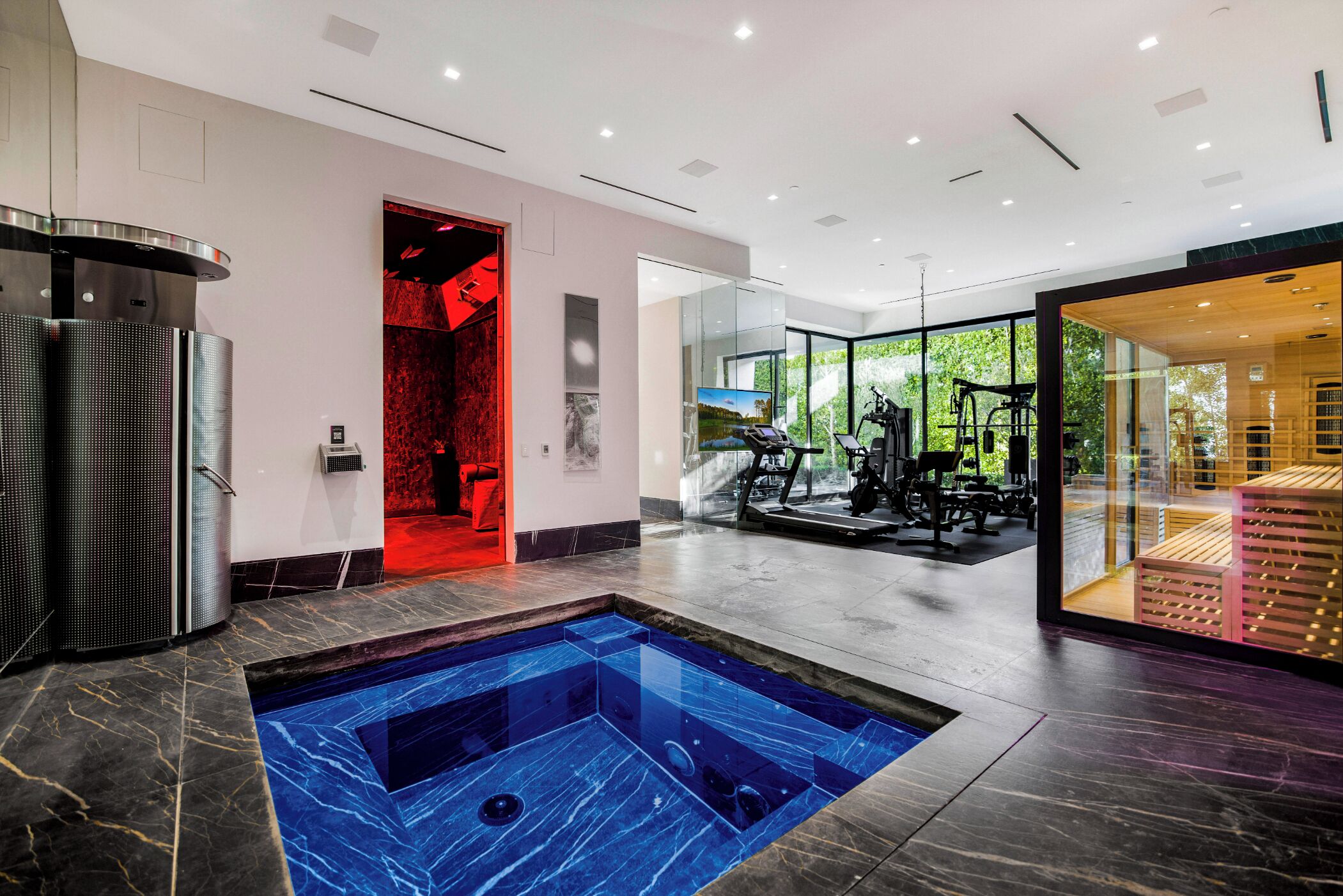 Ein moderner Wellnessbereich mit Whirlpool, Fitnessgeräten und einem durch Glas abgetrennten Raum.